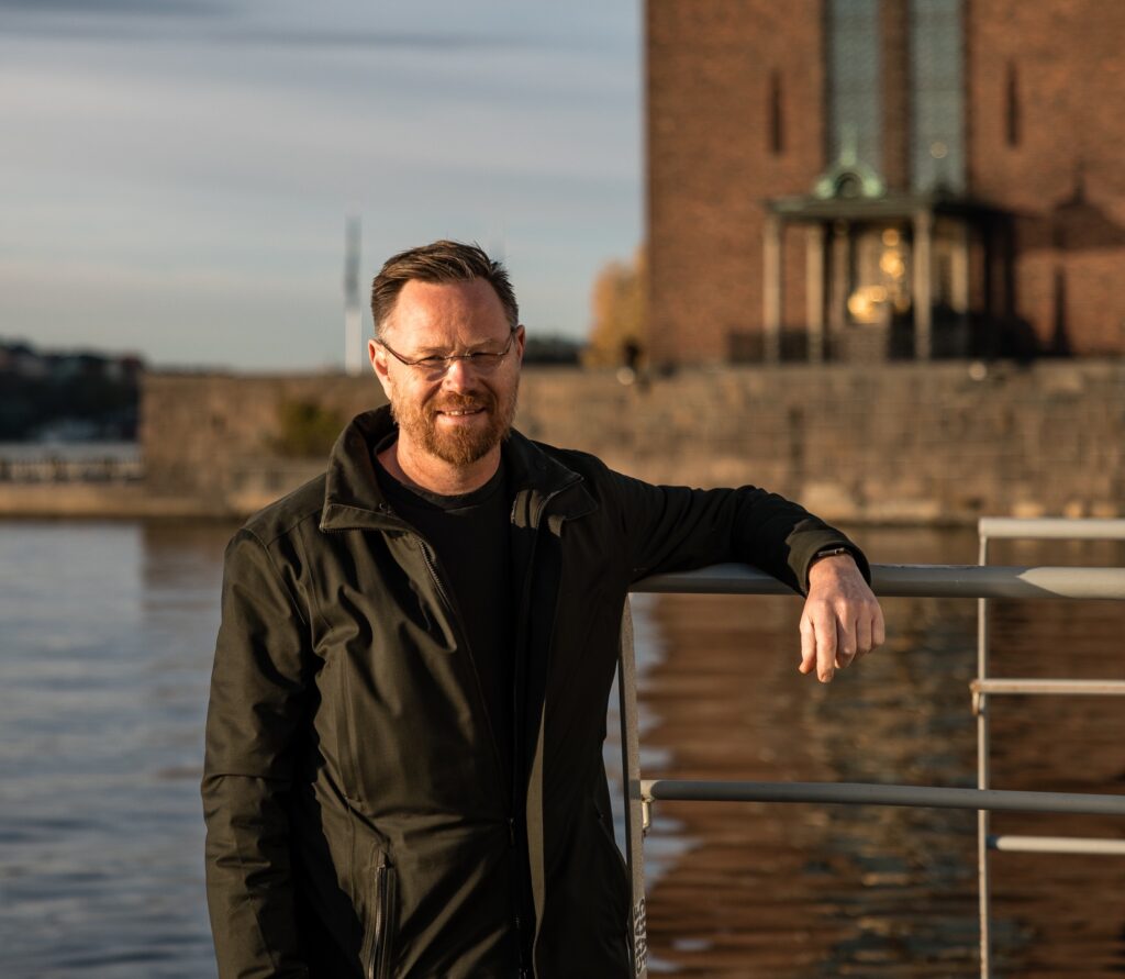 man looks at camera as he stands in from of water in Stockholm - it's Gustav Hasselskog CEO and founder of Candela