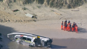 Aerial view of rescue boat washed up on beach with rescue personnel standing nearby